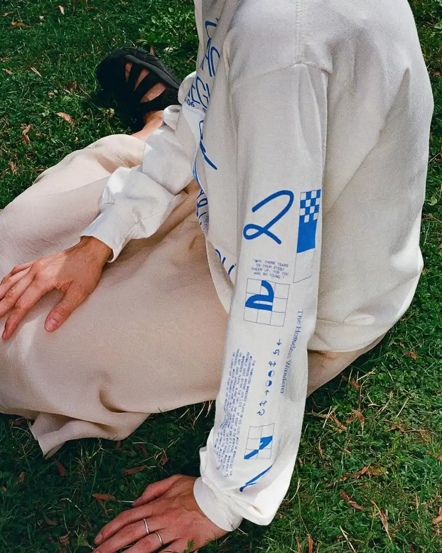 A cream long sleeve with a blue sleeve print, worn on the grass